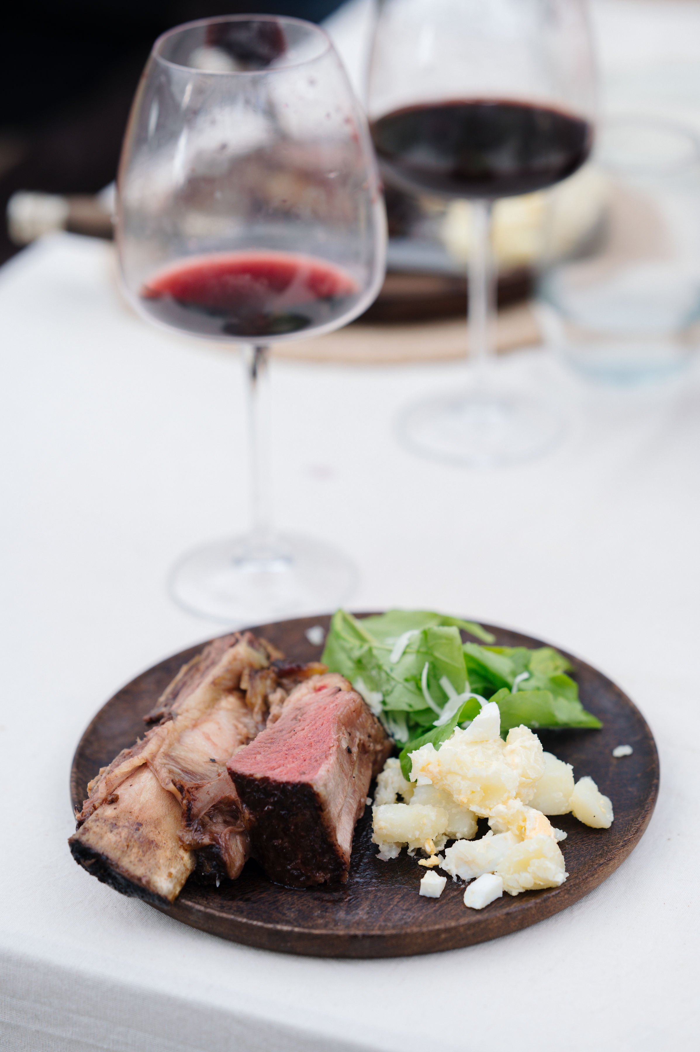 Plato de asado con ensalada y copas de vino tinto